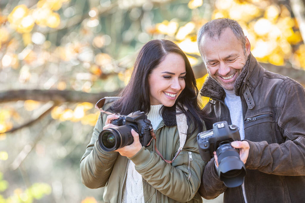 Professional photographer teaches photography to his student outdoors, both smiling at the picture in his camera. - Photo, image