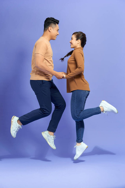 Привлекательные партнеры держась за руки прыжки весело изолированы на фиолетовом фоне - Фото, изображение