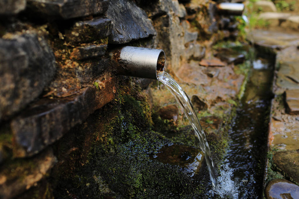 água de nascente derramando de um tubo de metal de uma parede de pedra nas florestas nas montanhas. - Foto, Imagem
