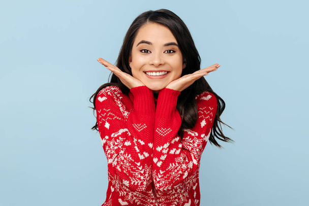 Cheerful young brunette woman dressed in Christmas sweater smiling over blue background. - Fotografie, Obrázek