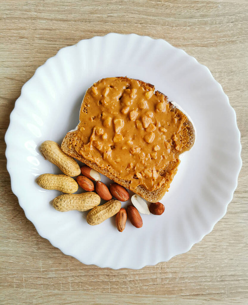 Sanduíche de manteiga de amendoim e amendoim em uma placa branca sob luz solar brilhante. Manhã comida café da manhã - Foto, Imagem