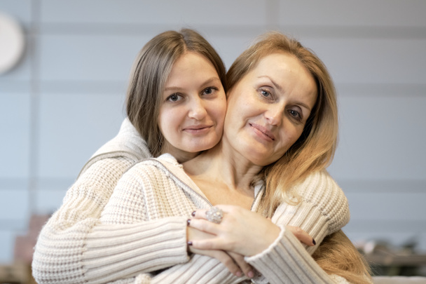 Beautiful family of mother and daughter together, hugging and kissing at home. senior mom and her adult daughter are hugging, looking at camera and smiling - Foto, afbeelding