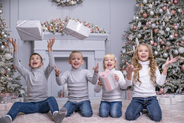 2人の男の子と2人の女の子はクリスマスの装飾が施された部屋でクリスマスプレゼントを投げます。とても面白いですね. - 写真・画像