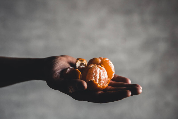 Ripe juicy sweet orange mandarins in a human hand against a dark background. - Фото, зображення
