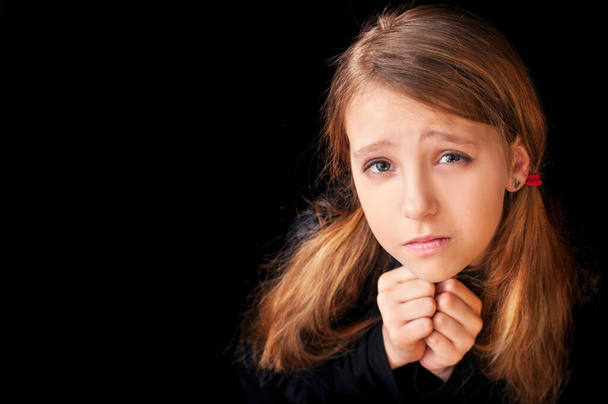 Портрет молодой девушки на черном фоне. Она молитвенно молилась. Она просит Бога о помощи. Горизонтально. Копирование пространства - Фото, изображение