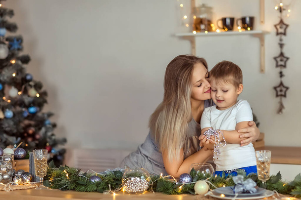 A smiling young girl and a boy sit at a table in a decorated Christmas kitchen. Selective focus. Homemade cakes, Christmas sweets, winter holiday concept. - Fotoğraf, Görsel