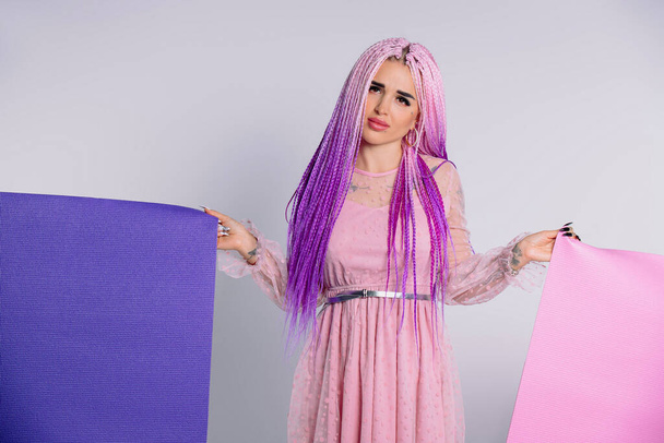 Sad girl with pink hair in a dress and with two upturned yoga mats. White background. High quality photo - Zdjęcie, obraz