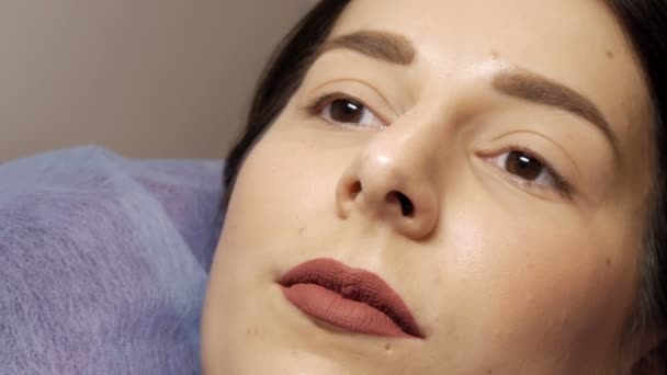 Close-up rosto de uma jovem antes de um procedimento moderno de laminação de pestanas em um salão de beleza profissional antes do procedimento de ondulação de pestanas. Retrato de uma mulher sem maquiagem com batom escuro - Filmagem, Vídeo