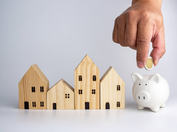 A model wooden house and a man's hand holding a coin On a white background. Housing business concept. - Photo, Image