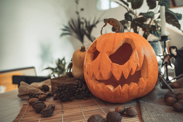 Halloween spooky pumpkin face with candle lit in a table and sun light. Skeleton, candles, nuts. Teal and orange beautiful still life. - 写真・画像