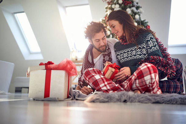 A young couple got up from bed and opening Xmas presents on a beautiful holiday morning. Christmas, relationship, love, together - Photo, image