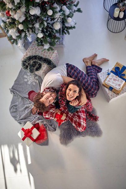 Egy kedves pár karácsonyi ajándékokkal pózol egy fotón egy gyönyörű ünnepi reggelen otthon. Karácsony, kapcsolat, szerelem, együtt - Fotó, kép