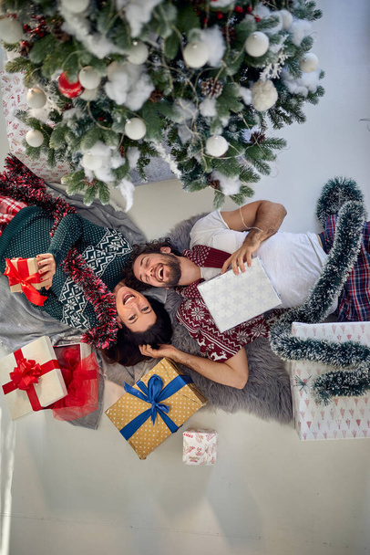 A lovely couple lying on the floor at home surrounded by Xmas presents on a beautiful holiday morning. Christmas, relationship, love, together - Foto, Imagen