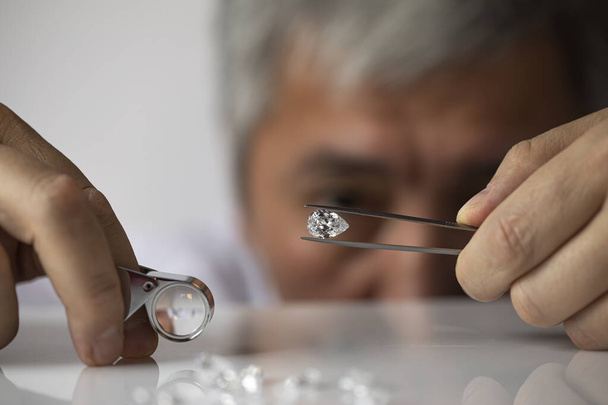 Man jeweller looking at diamond. Big brilliant in hand. Closeup diamond view. Luxury gem handling. - Foto, Bild
