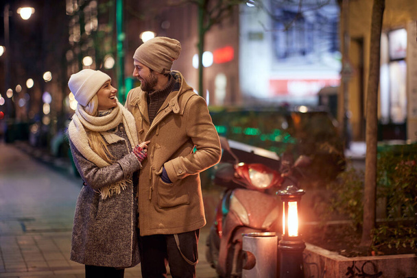 Una joven pareja feliz en la acera en una noche fría. Relación, juntos, Navidad - Foto, imagen