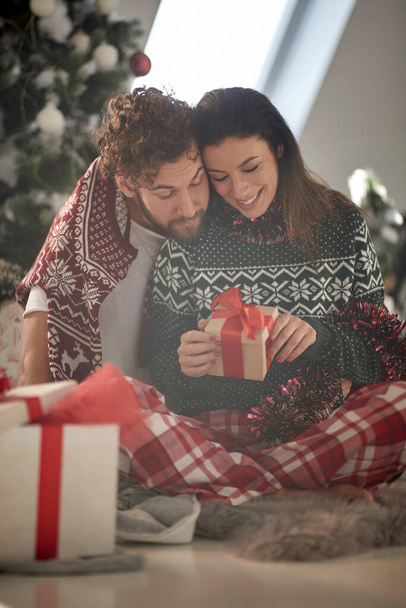 A young couple in love at home curious about Xmas presents on a beautiful holiday morning. Christmas, relationship, love, together - Fotografie, Obrázek
