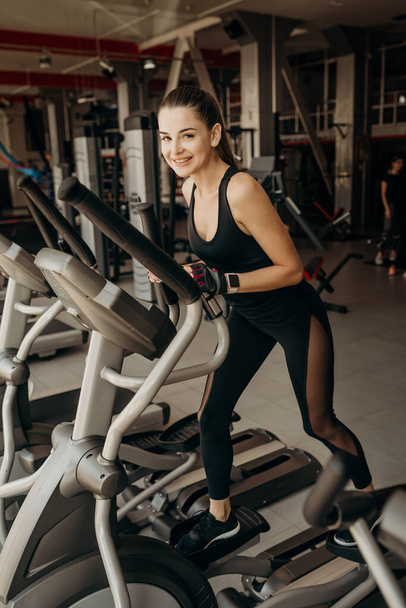 Young fit woman using an elliptic trainer in a fitness center - Photo, image