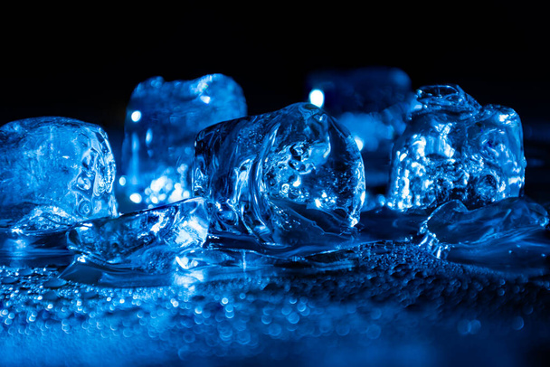 Танення заморожених кубиків льоду, освітлених синім кольором світлодіодного світла в темряві
. - Фото, зображення