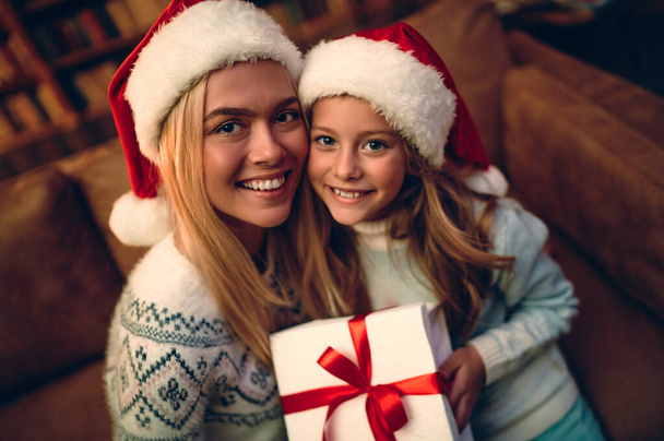 メリークリスマスとハッピーホリデー!陽気な母親とかわいい娘の女の子は贈り物を交換します。屋内で木の近くで遊んでいる親と小さな子供。プレゼント付きの家族を愛する. - 写真・画像