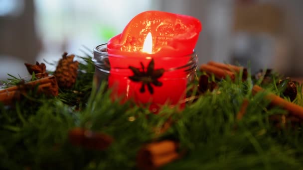 Primo piano di una corona d'avvento con candela di Natale in fiamme. Candela di Natale rossa all'interno di una corona d'avvento. - Filmati, video
