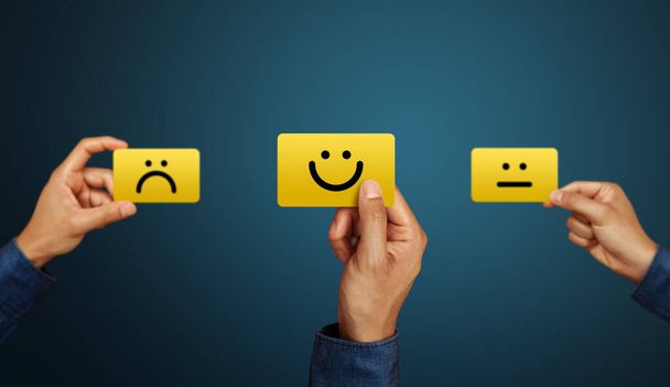 Die Hand des Kunden zeigt ein Feedback mit Smiley-Gesichtskarte. Leistungsbewertung, Zufriedenheitskonzept - Foto, Bild