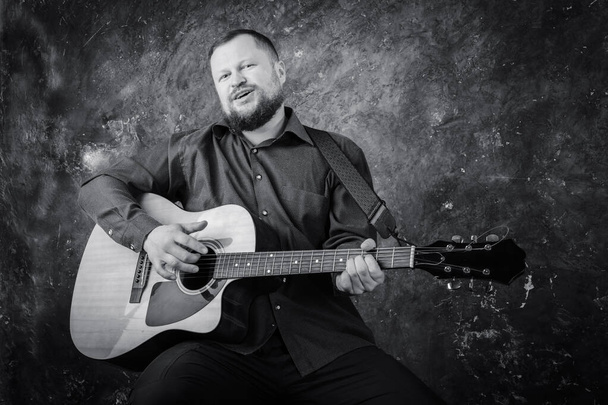 Mature musician plays acoustic guitar emotional studio portrait. - Фото, изображение