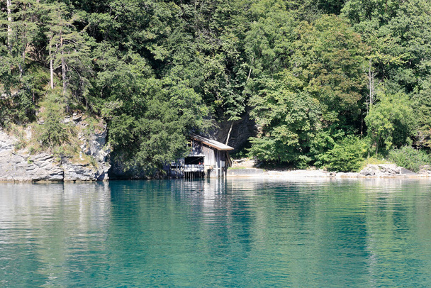 A Lucerne-tó partján lévő kis épület úgy néz ki, mintha a fák között rejtőzne. Ezek a fák beborítják a hegy meredek lejtőjét.. - Fotó, kép