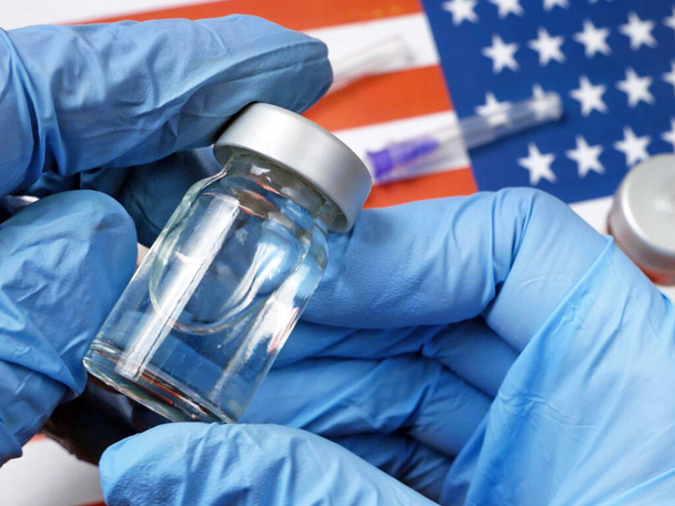 Пляшка вакцини утримується вручну в рукавичці на задньому плані прапора США, вакцина проти коронавірусу. - Фото, зображення