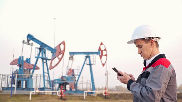 travailleur de l'industrie pétrolière avec téléphone sur le fond de la pompe à huile - Photo, image