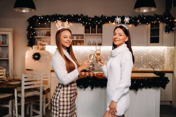two girls in a cozy home environment with champagne in their hands at Christmas. Smiling girls drink champagne on a festive evening. - Фото, зображення