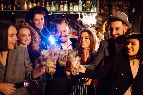 Group of friends cheering and drinking cocktails together at the bar. Young people celebrating winter holiday together with coctails at a nightclub party. Youth, lifestyle, drink, birthday concept. - Fotoğraf, Görsel