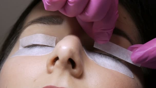 Modern eyelash lamination procedure in a professional beauty salon. The master sticks special adhesive patches on the eyes before the eyelash curling procedure - Footage, Video