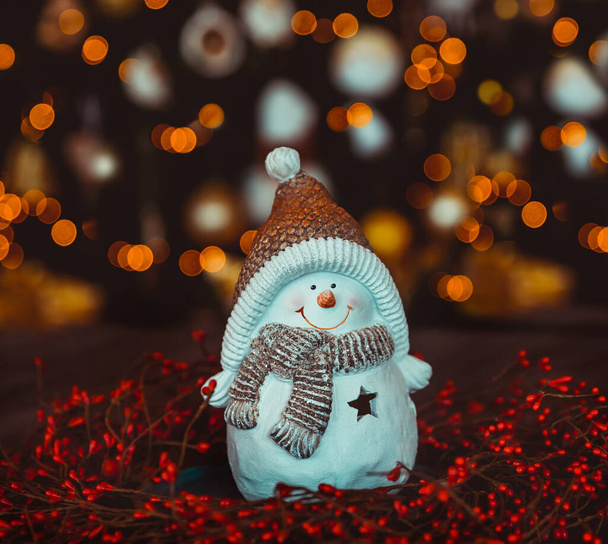 Nice Little Snowman Candlestick on the Table over Decorated Glowing Christmas Tree Bokeh Lights Background. Happy Winter Holidays at Home. Merry Christmas and Happy New Yea - Photo, Image