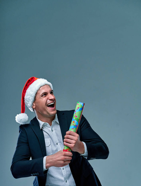 Successful man in a suit on a gray background in a cap of Santa Claus celebrates the New Year. Studio shooting. - Photo, Image