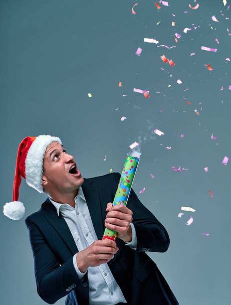 Successful man in a suit on a gray background in a cap of Santa Claus celebrates the New Year. Studio shooting. - Foto, Imagem