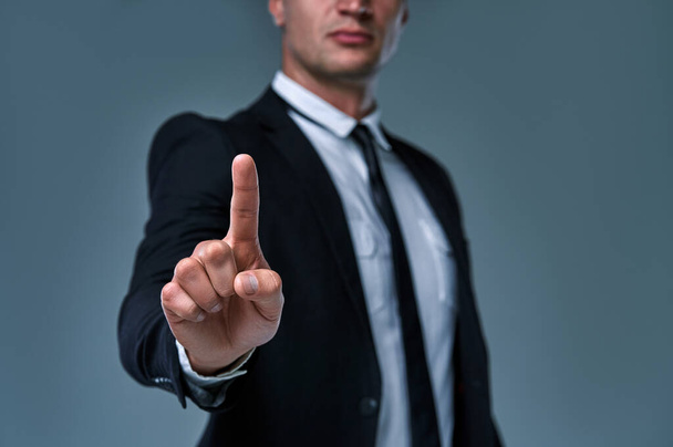Geschäftsmann mit Zeigen auf etwas oder Berühren eines Touchscreens auf grauem Hintergrund. - Foto, Bild