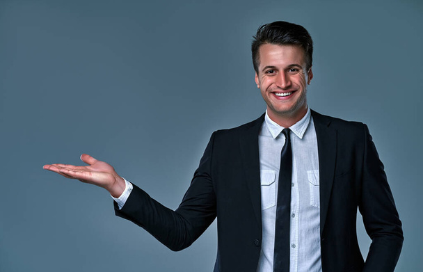 Close-up portrait of his he nice attractive cheerful cheery businessman agent broker wearing black suit holding invisible object on palm advert decision isolated over gray background. - Photo, Image