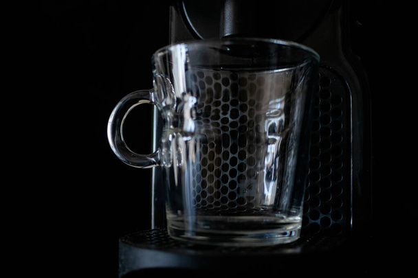 Átlátszó üveg pohár egy eszpresszó gépben. Koncepció, pihenés. Sötét háttér - Fotó, kép