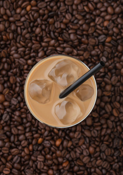 Glas kalten Kaffees mit Eiswürfeln und Stroh auf frischem Rohkaffee Hintergrund. Ansicht von oben - Foto, Bild