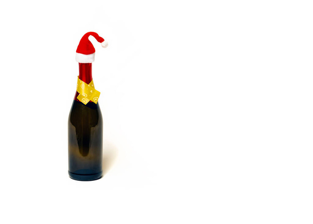 Butelka szampana w kapeluszu Mikołaja. Butelka szampana z czerwonym świątecznym kapeluszem na białym tle. - Zdjęcie, obraz