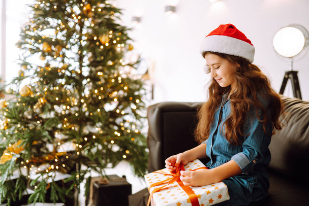 Happy female child in Santa red hat holding Christmas gifts. Smiling little girl posing with many presents in Christmas interior design. Winter holiday, New Year. - Foto, Imagem