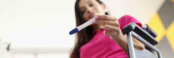 Vrouw in rolstoel zit en kijkt naar zwangerschapstest - Foto, afbeelding