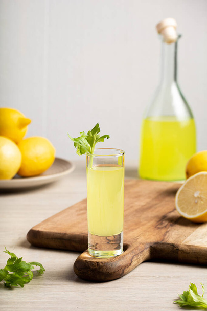 Licor italiano tradicional Limoncello. Botella de vidrio con licor casero de Limoncello, plato con limones y apio. - Foto, imagen