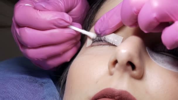 Face of young girl before eyelash lamination procedure in a professional beauty salon. The master washes off the black paint on the eyelashes during the eyelash curling procedure with a special brush - Footage, Video