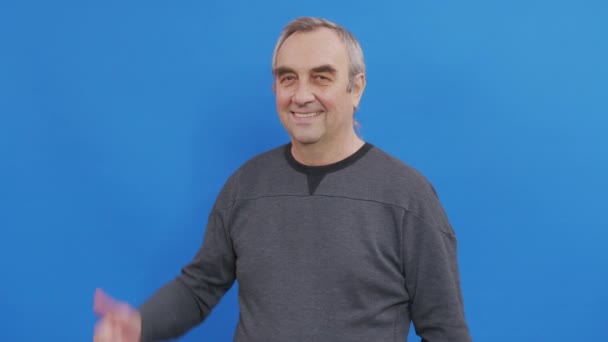 Senior man showing his thumbs up approving your choice. Studio shot on blue wall. - Footage, Video