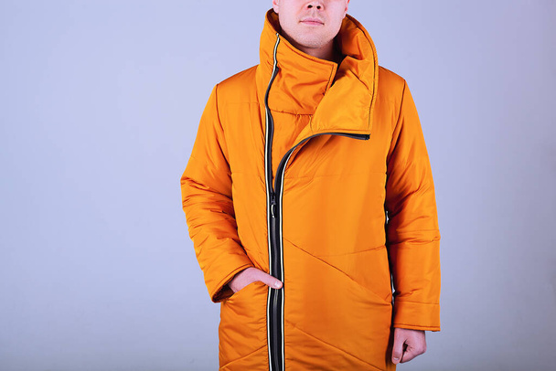 Modelo de hombre sobre un fondo gris vestido con una chaqueta naranja. La chaqueta está abotonada a mitad de camino. Una mano en el bolsillo. Barbilla blanca sin afeitar - Foto, imagen