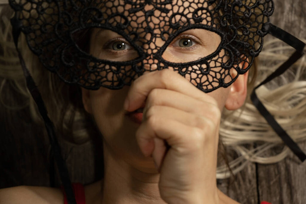 κορίτσι που κρατά μια μαύρη μάσκα καρναβαλιού μπροστά στο πρόσωπό της - Φωτογραφία, εικόνα