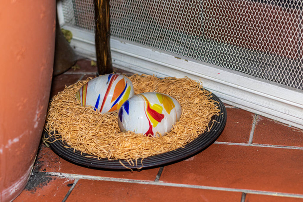 Sur une petite assiette avec des copeaux de bois, il y a deux objets en forme d'oeuf peints avec des peintures colorées. Composition pascale des œufs peints. - Photo, image