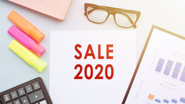 The text - SALE 2020 on office desk with calculator, markers, glasses and financial charts. - Foto, imagen