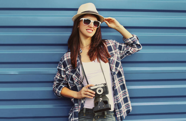 Portrait of young woman with film camera wearing a summer straw hat, shirt over a blue background - Valokuva, kuva